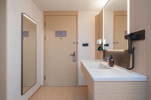 Un bagno moderno con una porta in legno, uno specchio grande, un lavandino bianco e un asciugacapelli fissato alla parete.