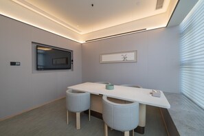 A modern meeting room with a long table, four grey cushioned chairs, recessed ceiling lighting, a mounted television, and a framed artwork on the wall. - Ji Hotel Guangzhou Huangpu East Metro Station (Guangzhou)