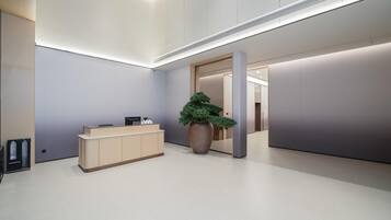 Un área de recepción moderna con un mostrador, una planta grande en maceta y un diseño interior minimalista.