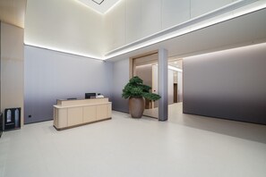 Egy modern fogadótér, amelyben található egy recepciós pult, egy nagy, virágzó növény és minimalista belsőépítészeti megoldások.