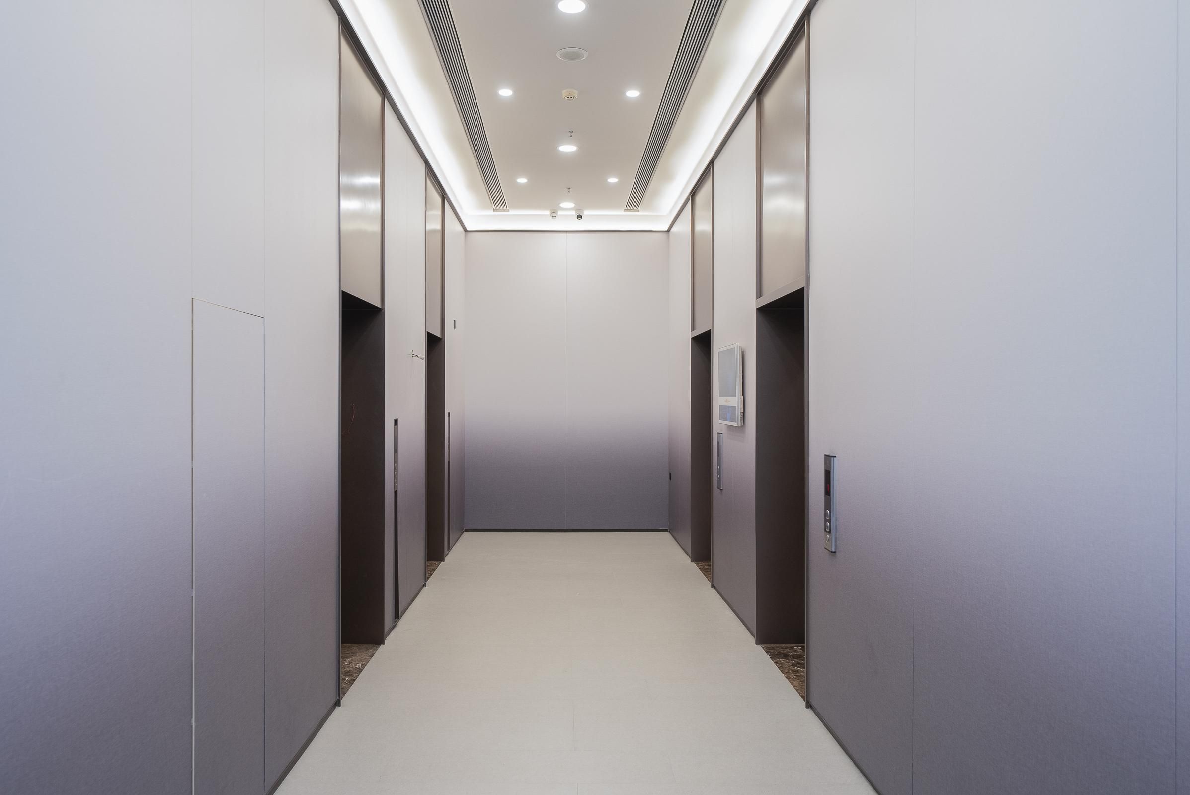 A modern elevator shaft with a clean, minimalist design, featuring a light-colored floor and walls, and a ceiling with recessed lighting.