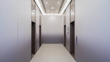 A modern elevator shaft with a clean, minimalist design, featuring a light-colored floor and walls, and a ceiling with recessed lighting.