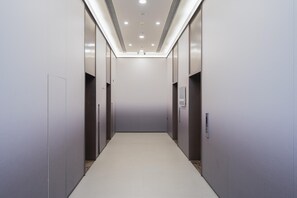 En modern hisschakt med en stilren och minimalistisk design, med ett ljust golv och ljusa väggar samt ett tak med infälld belysning.
