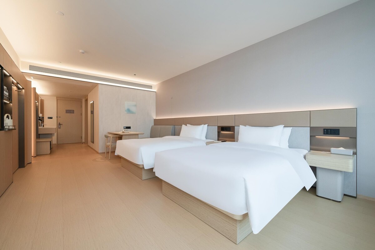 Ett modernt hotellrum med två sängar, ett skrivbord och en liten sittgrupp.