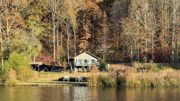 A cabin by a lake with a dock and chairs, surrounded by trees and a forest. - Cool villa on private lake with breathtaking views and perfect sunsets (Clarkesville)
