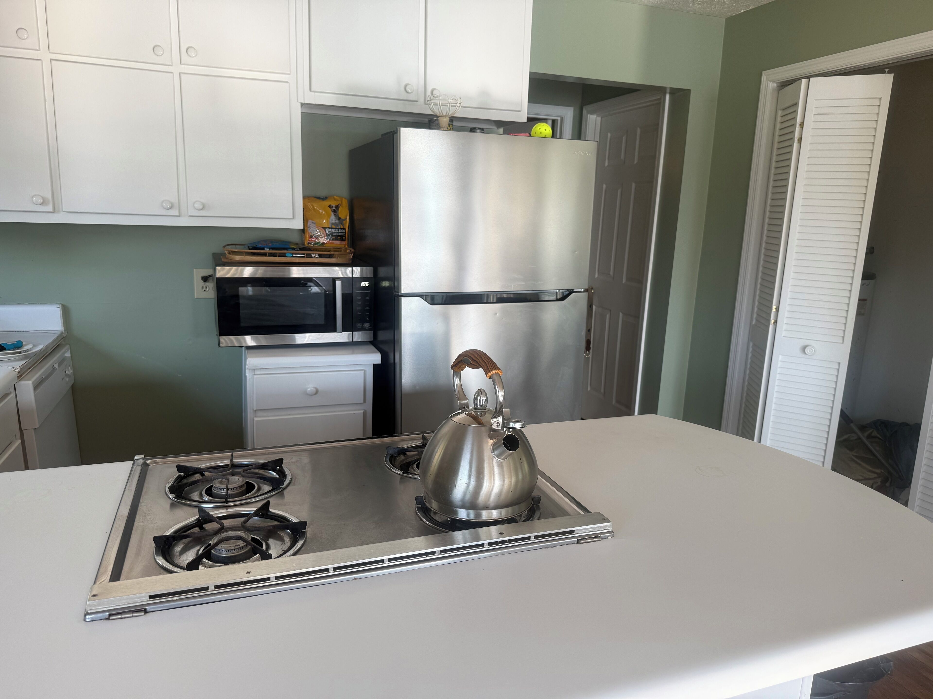A kitchen with a stainless steel refrigerator, microwave, kettle, and gas stove.