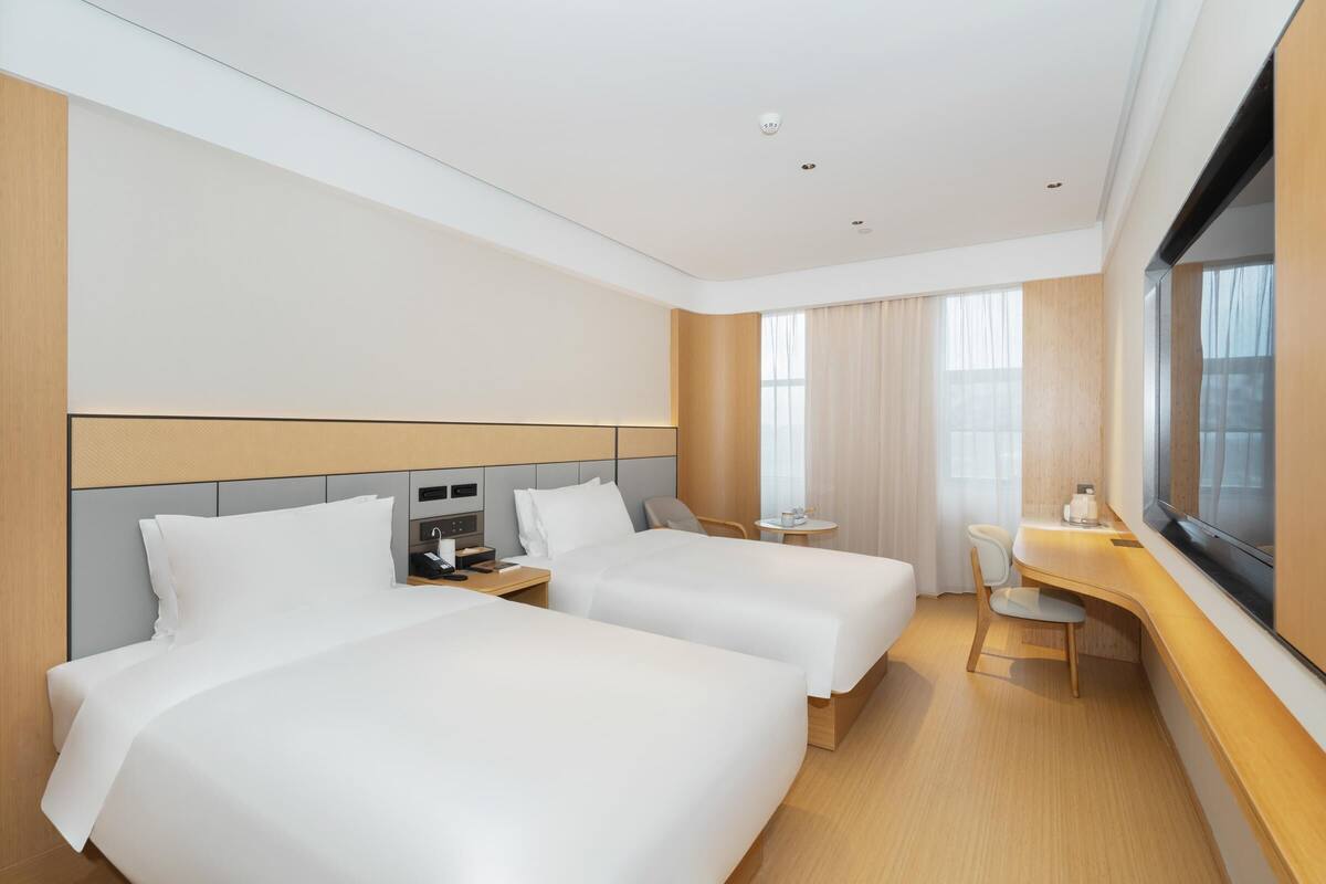 A hotel room with two beds, a desk, a chair, a small table, and a TV.