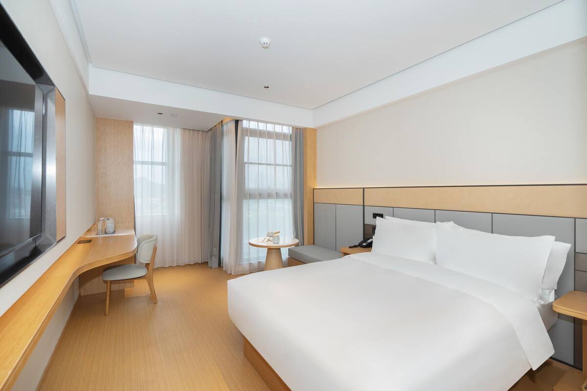 A modern hotel room with a large bed, a desk, a chair, and a small table.