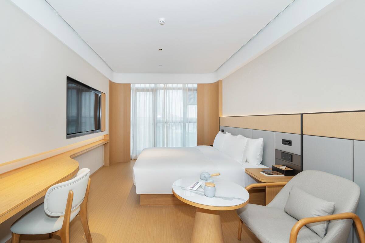 A modern hotel room with a large bed, a desk, a chair, and a small table.