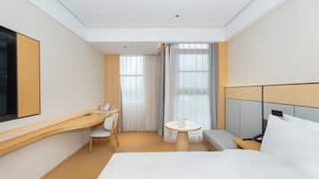A modern hotel room with a bed, a desk, a chair, a small table, and a TV.