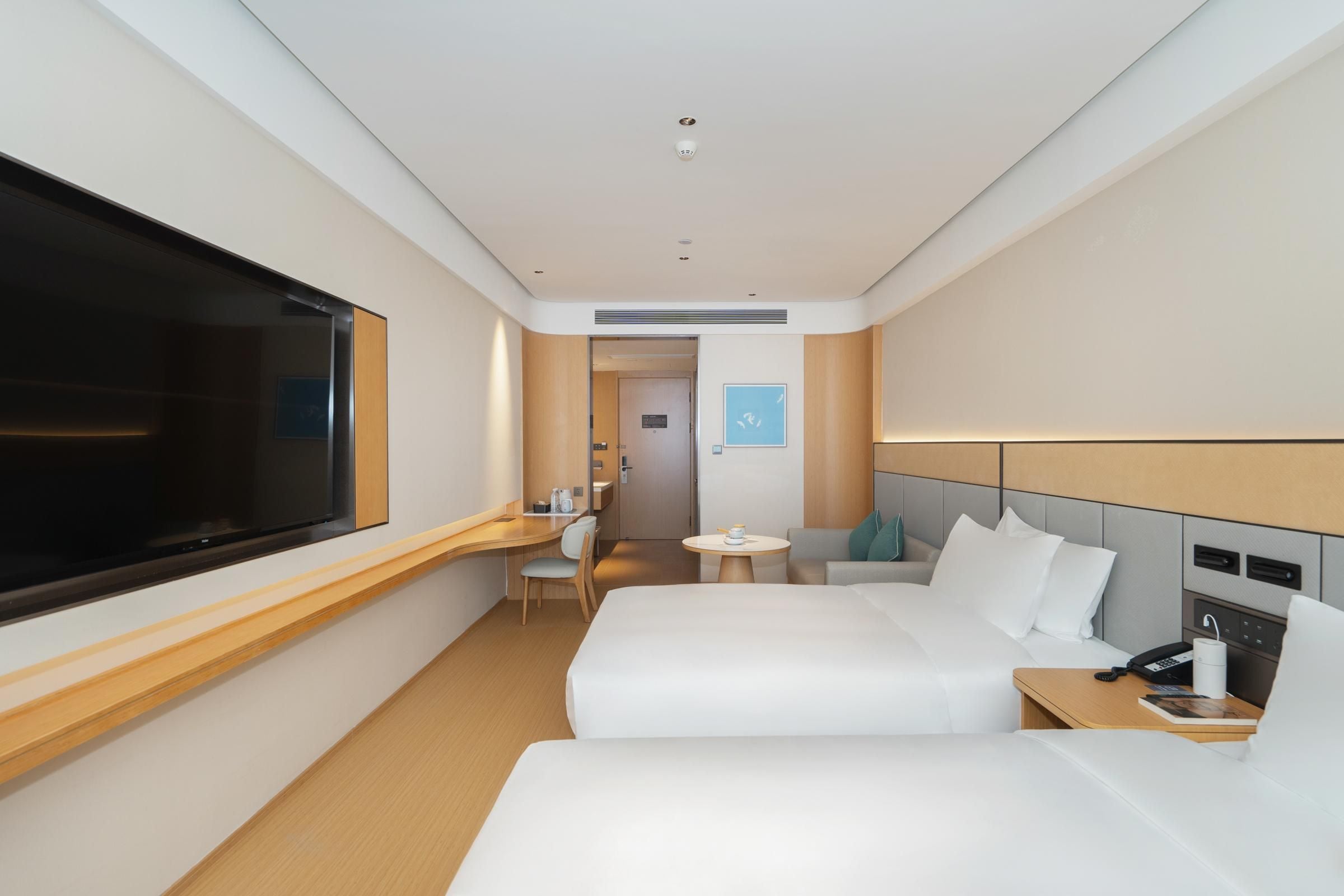 Een moderne hotelkamer met twee bedden, een bureau, een stoel, een klein tafeltje, een televisie en een telefoon.