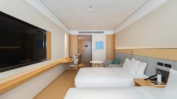Una habitación de hotel moderna con dos camas, un escritorio, una silla, una mesita, un televisor y un teléfono.