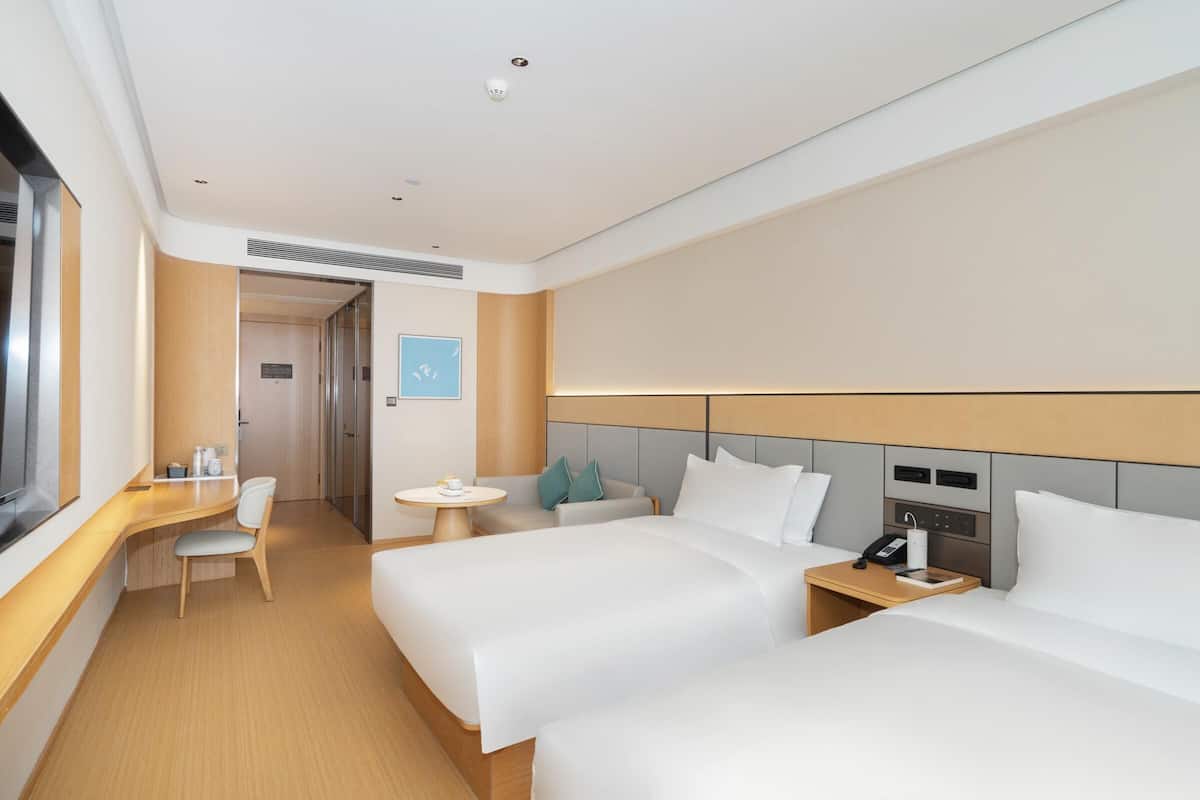 A hotel room with two beds, a desk, a chair, a small table, and a TV.