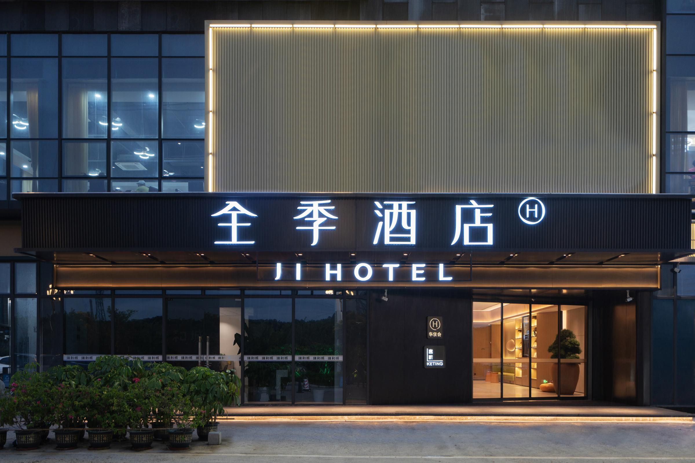 A hotel entrance with a modern facade, illuminated signage, and a visible entrance door.