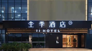 A hotel entrance with a modern facade, illuminated signage, and a visible entrance door.