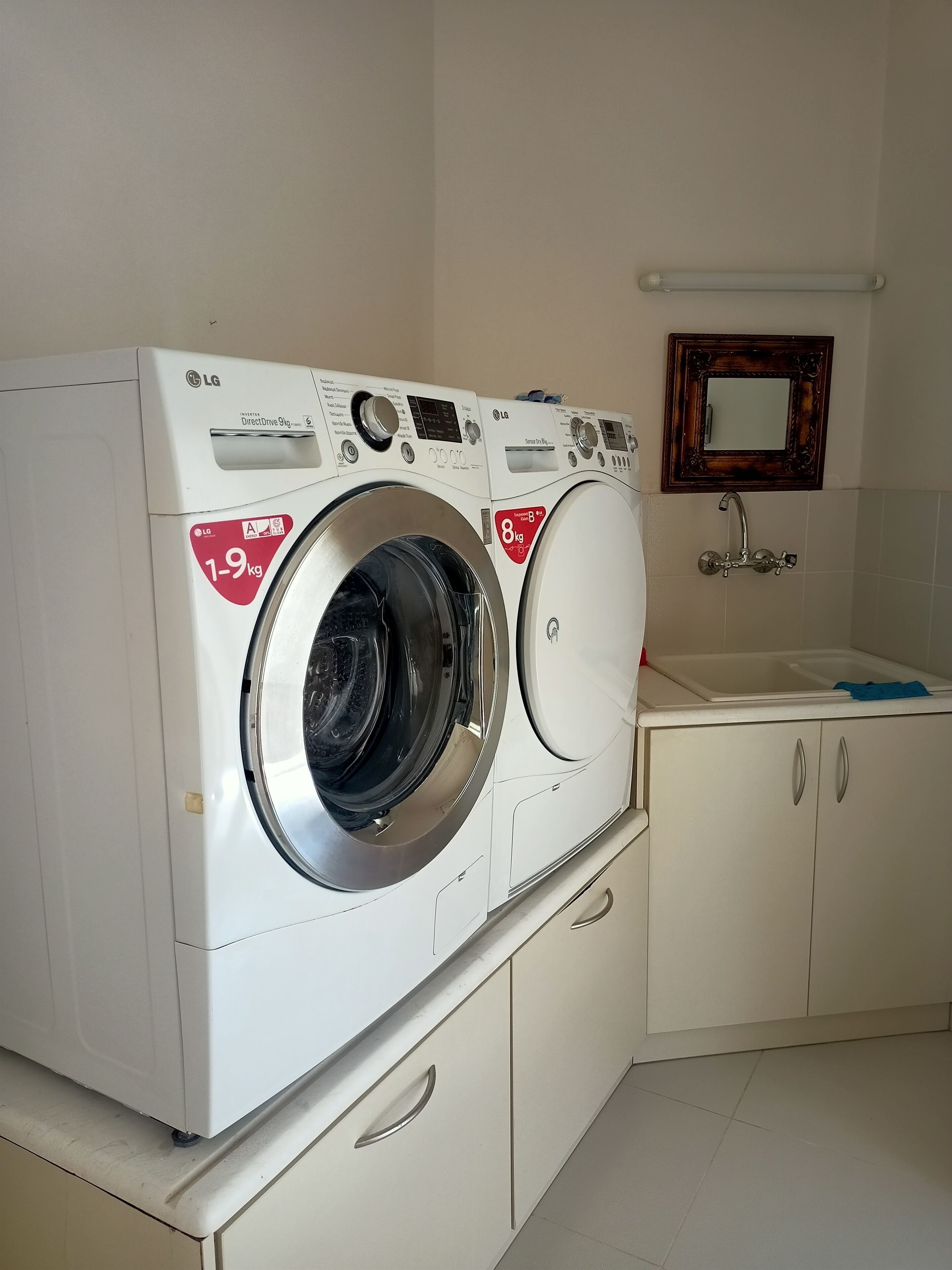 Zona de lavandería con dos lavadoras LG DirectDrive de 9 kg con carga frontal, un lavamanos y un espejo.