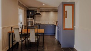 A compact kitchen with a dining area, featuring a wooden table and chairs, a built-in oven, and a blue cabinet. - Alpine Springs Motel | Unit 8 - HS61218 (Hanmer Springs)