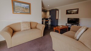 A living room with two sofas, a coffee table, a TV, and framed artwork on the walls. - Alpine Springs Motel | Unit 8 - HS61218 (Hanmer Springs)