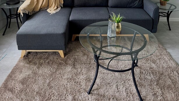 A modern living room with a grey sectional sofa, a glass coffee table, and a large abstract painting on the wall.