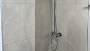 A shower with a handheld showerhead and a wall-mounted rain showerhead, set in a room with large, light-colored tiles.