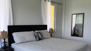 A neatly arranged bedroom with a large bed, two bedside tables with lamps, a ceiling fan, and a window with curtains.