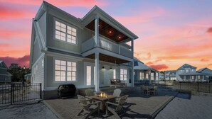 A two-story house with a covered patio and a fire pit. - Salt and Sand at Summer Salt | Zero Entry Pool | Beach Access | Lake Fishing | My Beach Getaways (Orange Beach)