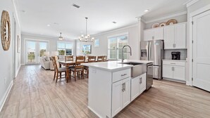 A spacious kitchen with white cabinetry, a central island, and a dining area with wooden chairs and a table. - Salt and Sand at Summer Salt | Zero Entry Pool | Beach Access | Lake Fishing | My Beach Getaways (Orange Beach)