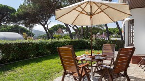A patio with a table and chairs, a large umbrella, and a view of a house and trees.