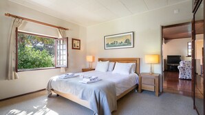 A bedroom with a bed, two bedside tables with lamps, a window with curtains, a painting on the wall, and a view of the outdoors.