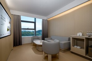 Ett modernt hotellrum med en soffa, stolar, ett litet bord, en tv-skärm och utsikt över bergen.