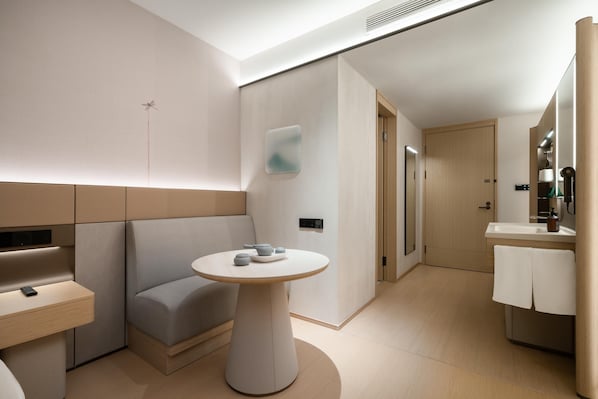 A modern hotel room with a minimalist design, featuring a sofa, a round table, a small bathroom with a sink and mirror, and a door leading to another room. - Ji Hotel Guangzhou Huangpu Science City Luogang (Guangzhou)