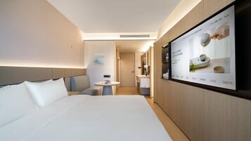 A modern hotel room with a large bed, a small table, and a TV mounted on the wall displaying a menu.