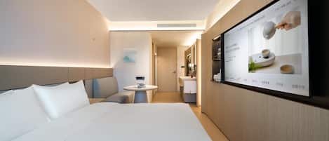 A modern hotel room with a large bed, a small table, and a TV mounted on the wall displaying a menu.