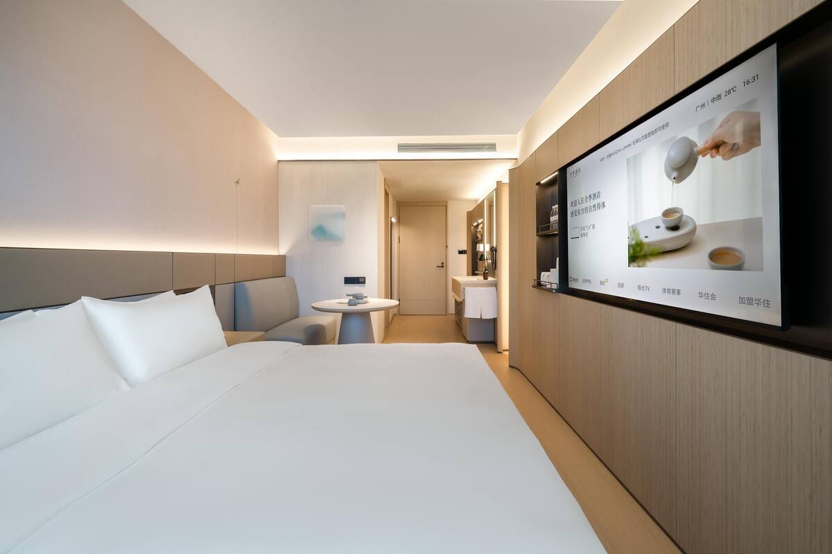 Ein modernes Hotelzimmer mit einem großen Bett, einem kleinen Tisch und einem an der Wand befestigten Fernseher, der eine Speisekarte zeigt.