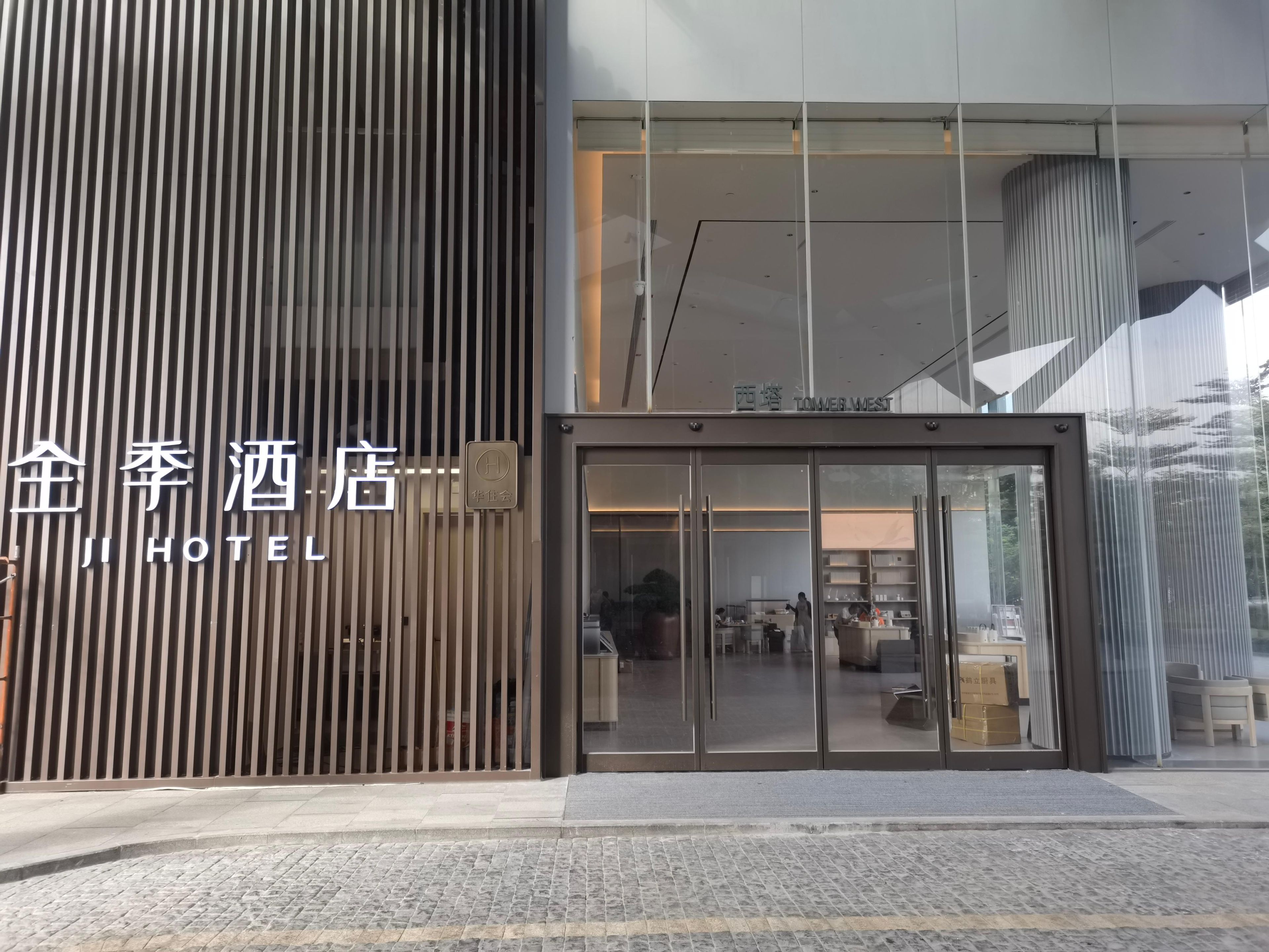 A hotel entrance with a modern design, featuring a vertical wooden panel and a glass door entrance.