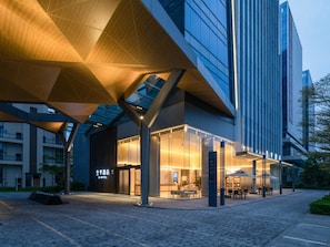 A modern hotel with a glass facade, outdoor seating area, and a distinctive wooden canopy structure. - Ji Hotel Guangzhou Huangpu Science City Luogang (Guangzhou)