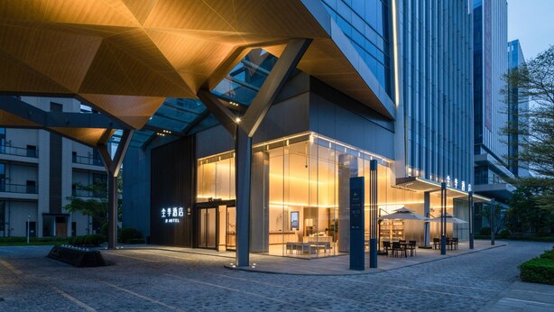 A modern hotel with a glass facade, outdoor seating area, and a distinctive wooden canopy structure. - Ji Hotel Guangzhou Huangpu Science City Luogang (Guangzhou)