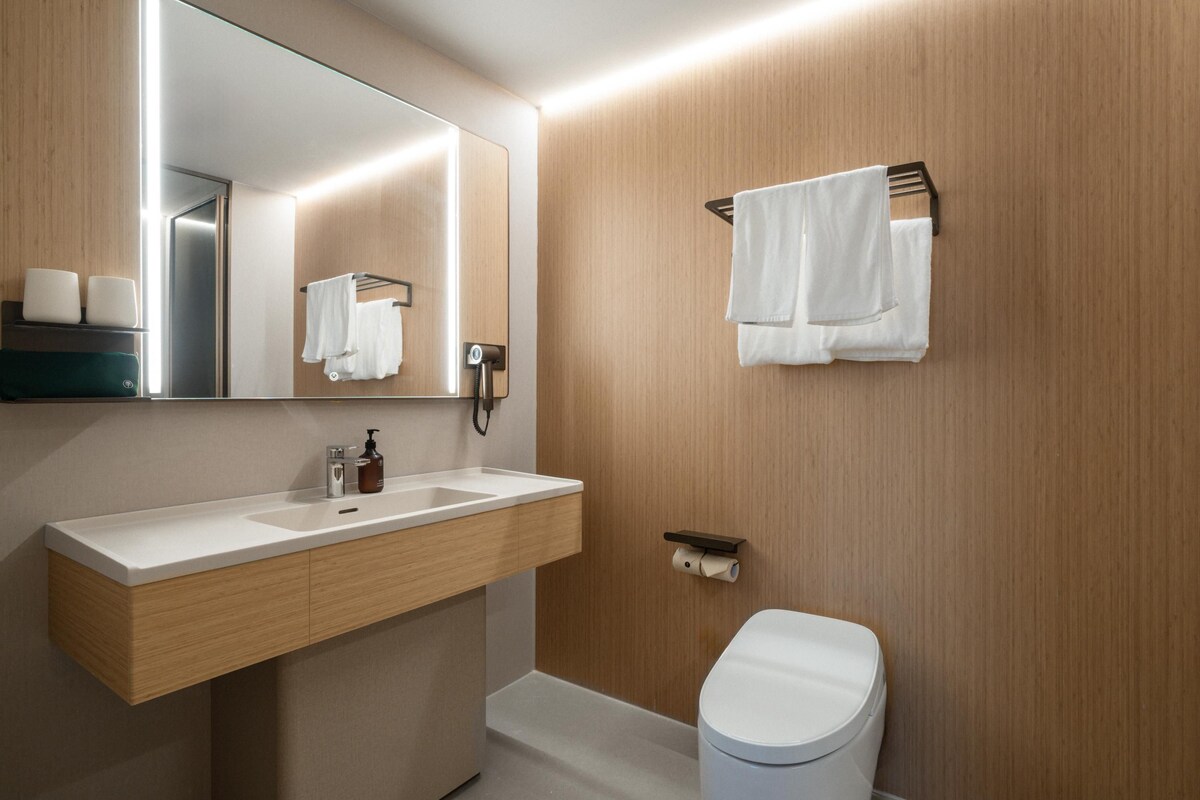 A modern bathroom with a wooden vanity, a mirror, a toilet, and a towel rack.