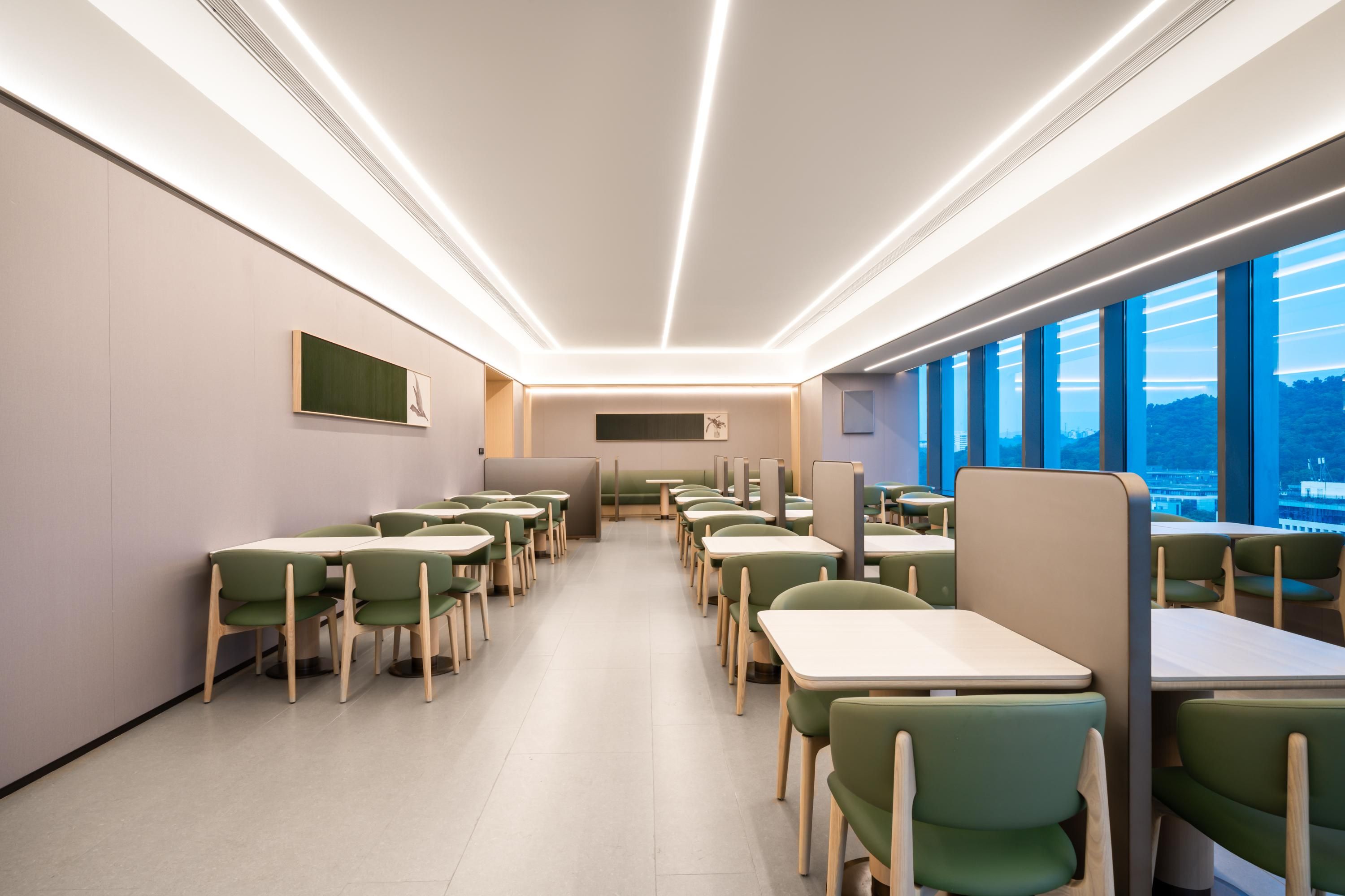 A modern dining area with long tables and green chairs, featuring a view through large windows.