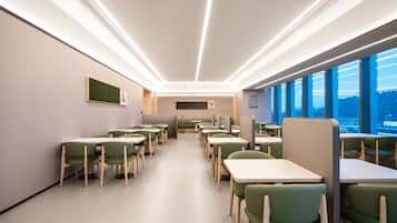 A modern dining area with long tables and green chairs, featuring a view through large windows.