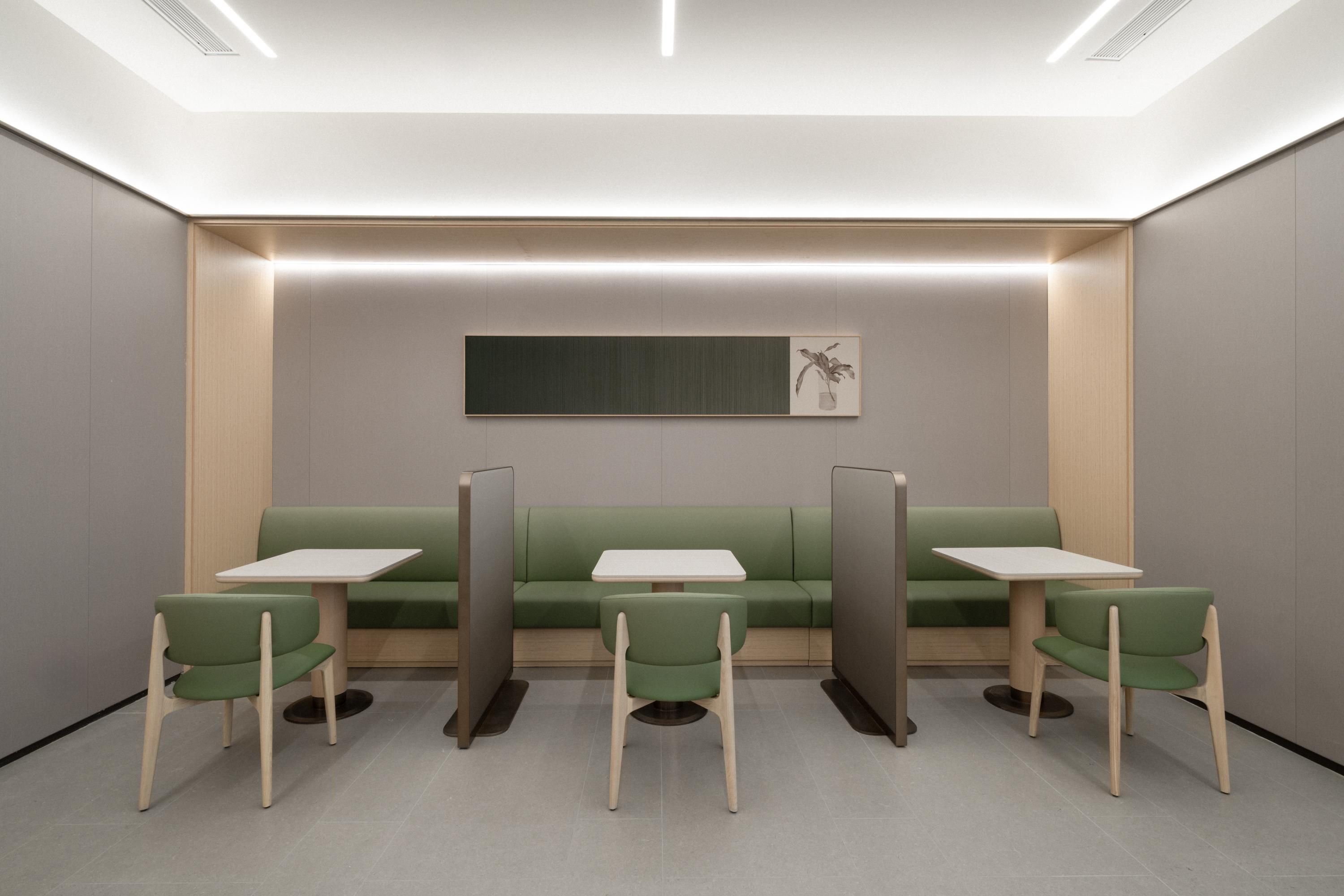Et moderne, minimalistisk venteområde med grønne siddepladser og hvide borde, præget af en neutral farvepalette og indbygget belysning.