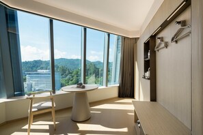 Una habitación de hotel moderna con ventanas amplias, una mesa redonda, una silla, un banco y un armario con perchas.