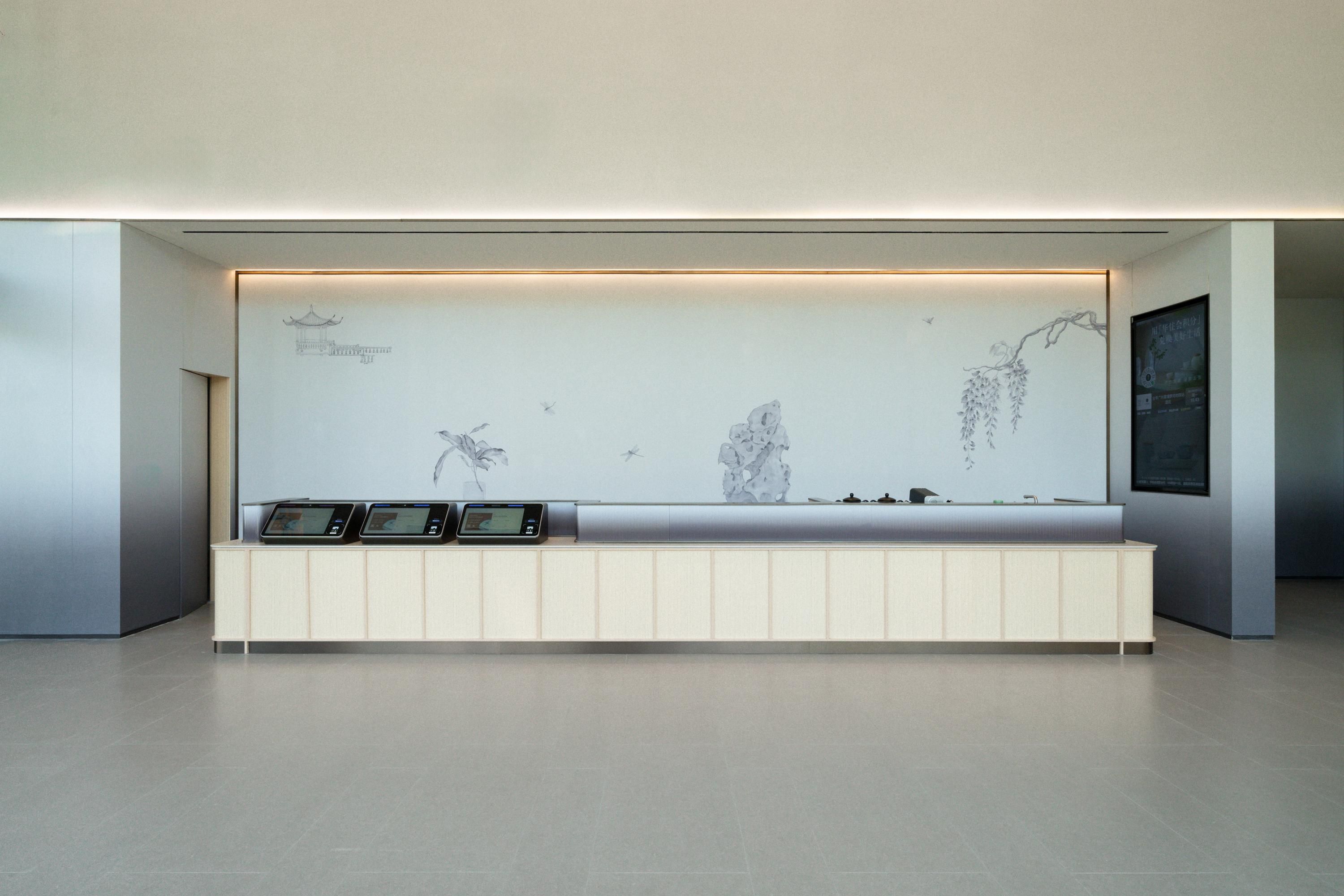 A reception area with a minimalist design, featuring a reception desk with digital displays and a wall-mounted screen displaying artwork.