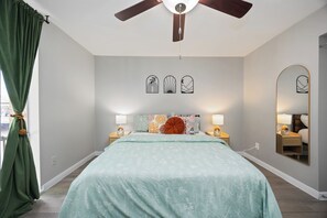 A bedroom with a bed, ceiling fan, bedside lamps, a mirror, and artwork on the wall.