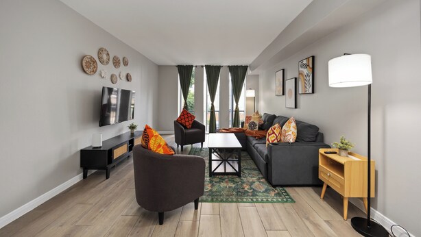 A modern living room with a sofa, armchair, TV, and floor lamp.