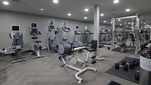 A gym with various exercise machines, including treadmills and weight stations, and a large mirror reflecting the equipment.