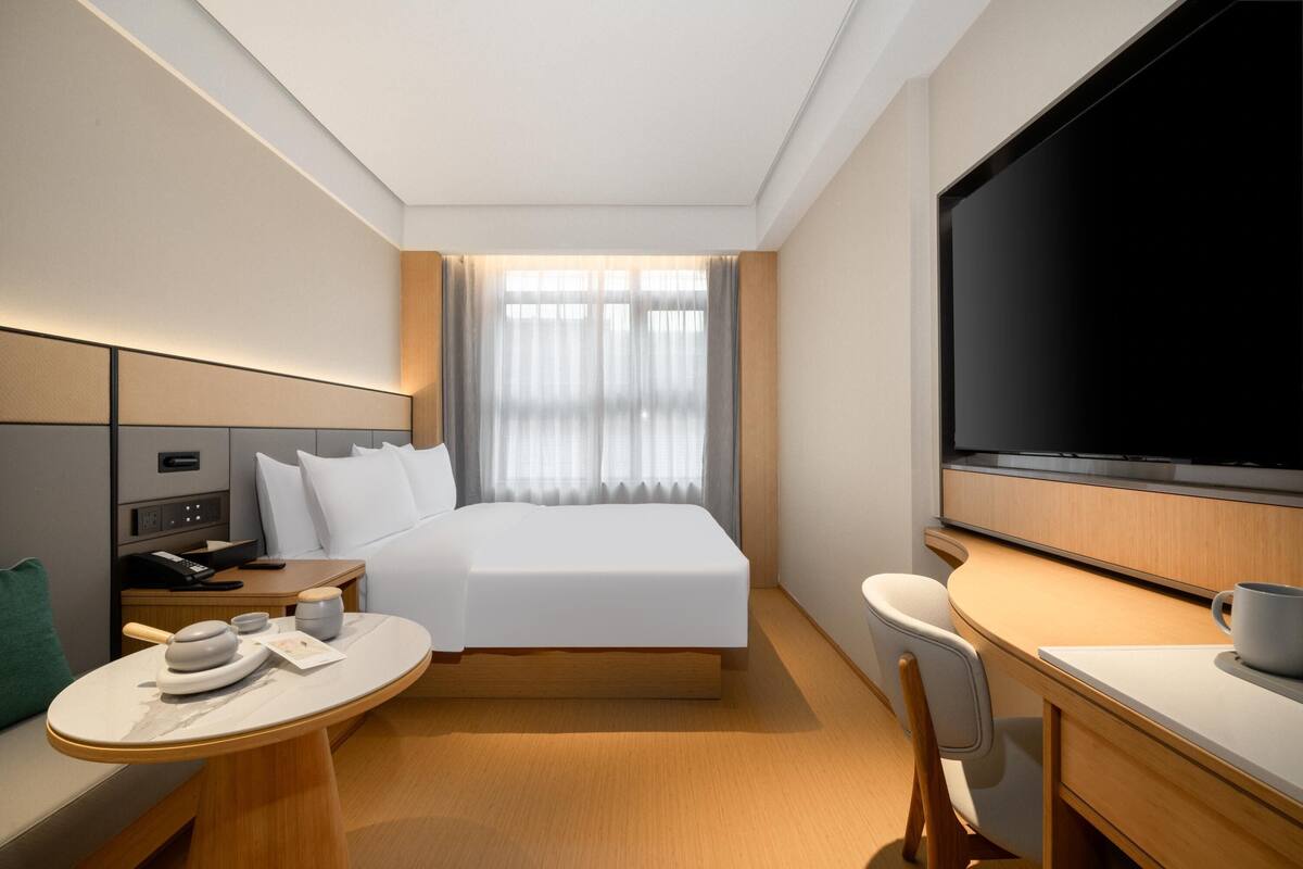A hotel room with a bed, a desk, a chair, a television, and a window with curtains.
