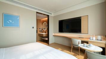 Una camera d'albergo moderna con un letto grande, una scrivania con televisore a schermo piatto, un tavolino rotondo e una sedia.