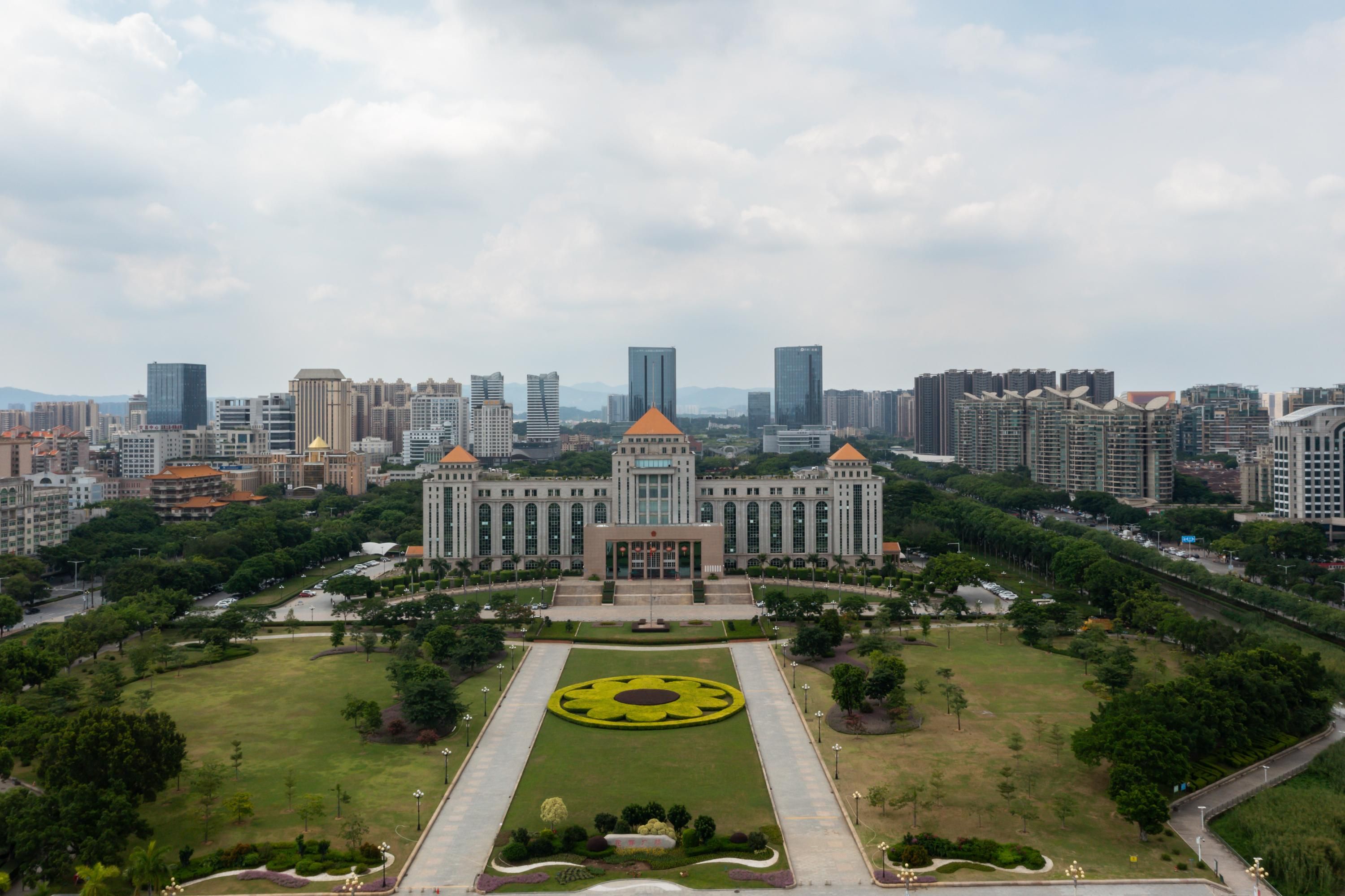 A large building with a central courtyard and surrounding greenery, surrounded by high-rise buildings.