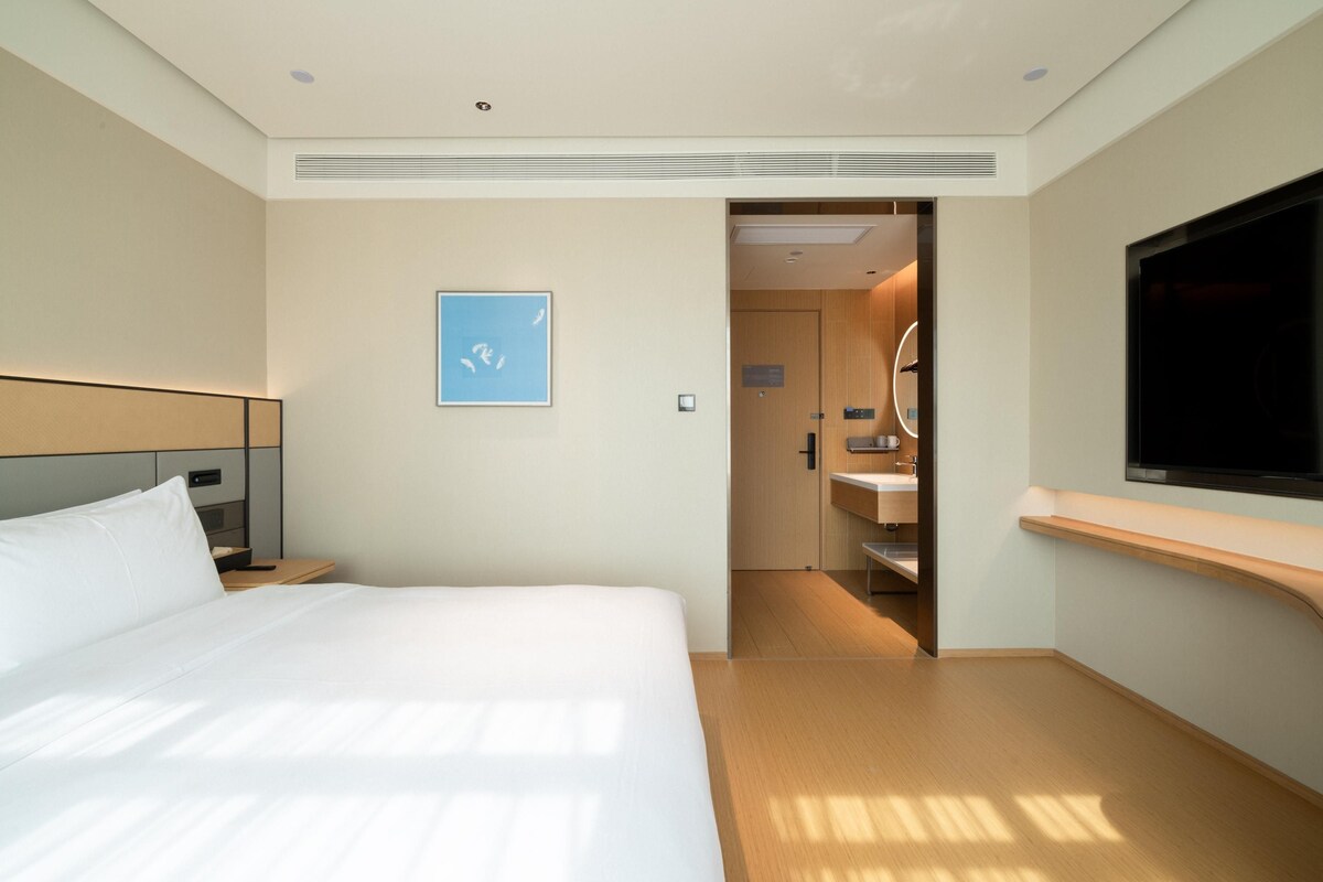 A hotel room with a bed, a TV, a bathroom with a sink and mirror, and a door leading to another room.